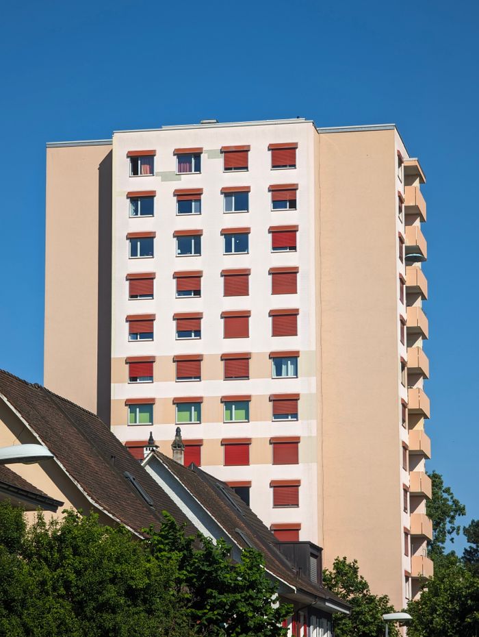 A contemporary apartment building with red window shutters against a clear blue sky.